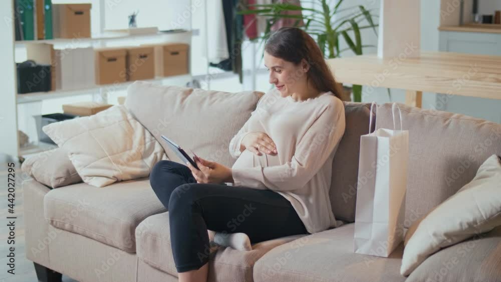 Young Pregnant Woman Uses a Modern Device, Buys Products for a Baby, Searches for Useful Information on the Internet, Online Delivery Order Concept. Young Pregnant Woman Uses a Modern Device, Buys Products for a Baby, Searches for Useful Information on the Internet, Online Delivery Order Concept.