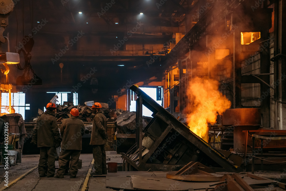 Steel production at metallurgical plant, workshop with unrecognizable workers and underground blast furnace.