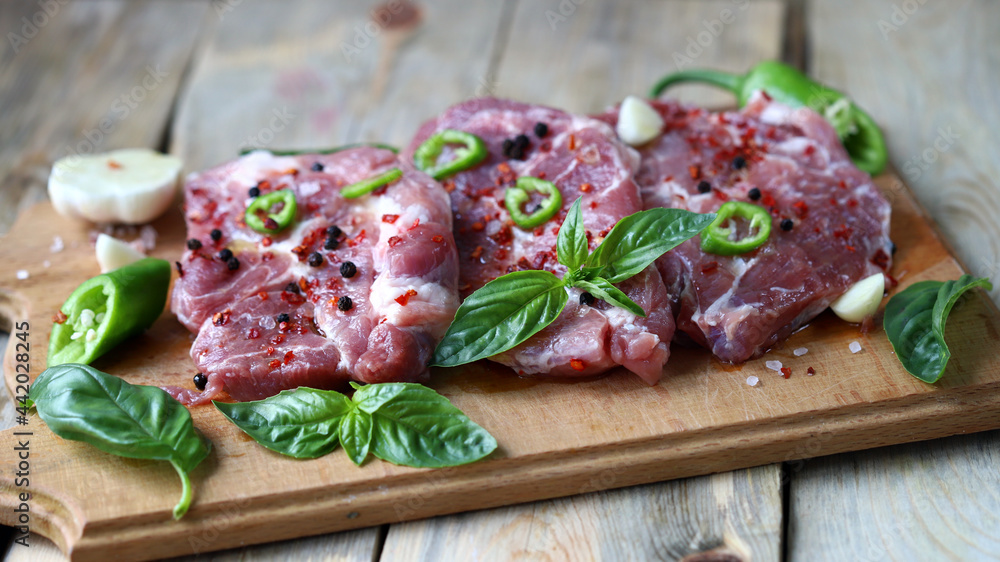 Raw pork steaks with spices on a wooden board. Raw pork steaks with spices on a wooden board.