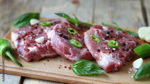 Raw pork steaks with spices on a wooden board.