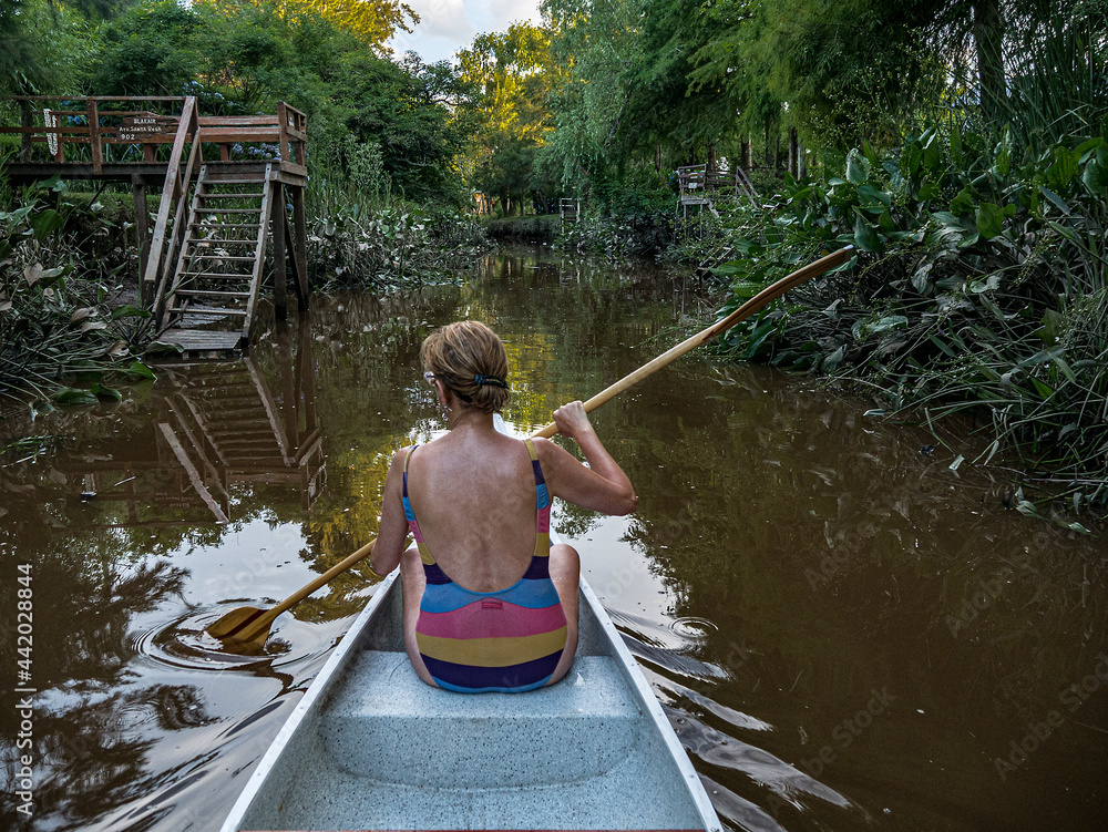 Sixties woman in a bathing suit paddles a canoe down a river in the
