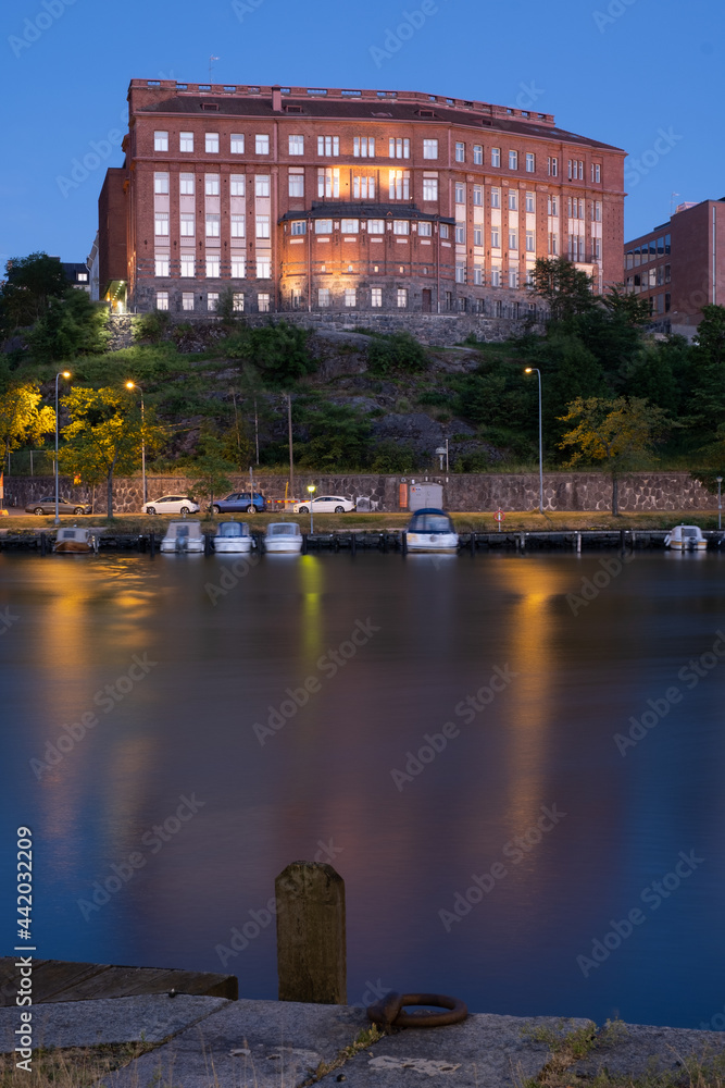 An old red brick building standing on the top of a hill. City lights casting reflections on the water.