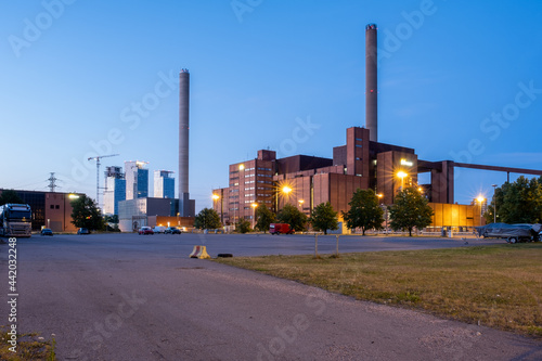 An old power plant with two smoke stacks. Modern skyscrapers in the background.
