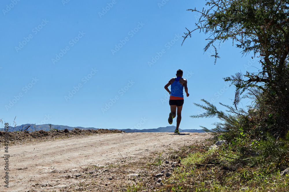 Latino man running a race on a rural road during summer. Crosscountry race. Copy space.
