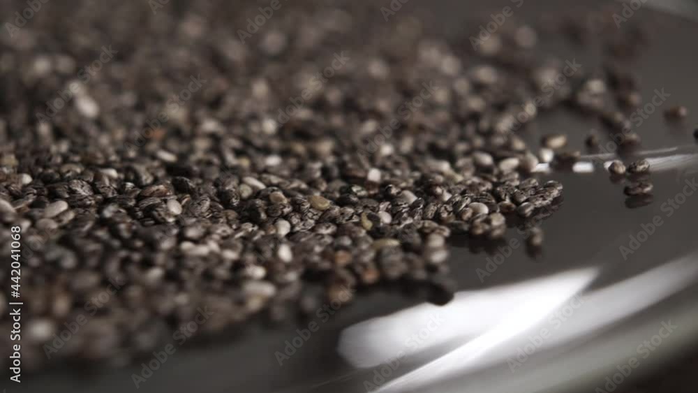 Chia seeds fall in slow motion on a shiny saucer. Macro. Rotation. Salvia hispanica. Healthy food concept Chia seeds fall in slow motion on a shiny saucer. Macro. Rotation. Salvia hispanica. Healthy food concept
