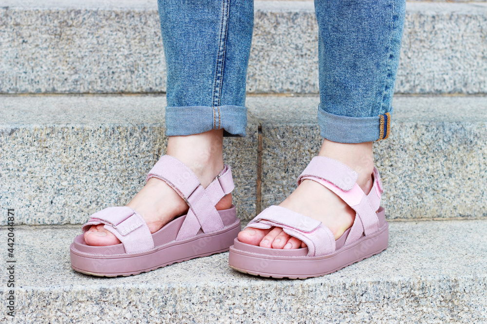 Female feet in pink sandals on on concrete staircase background close-up.