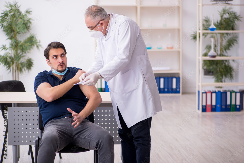 Obraz premium Young male patient visiting old male doctor in vaccination conce