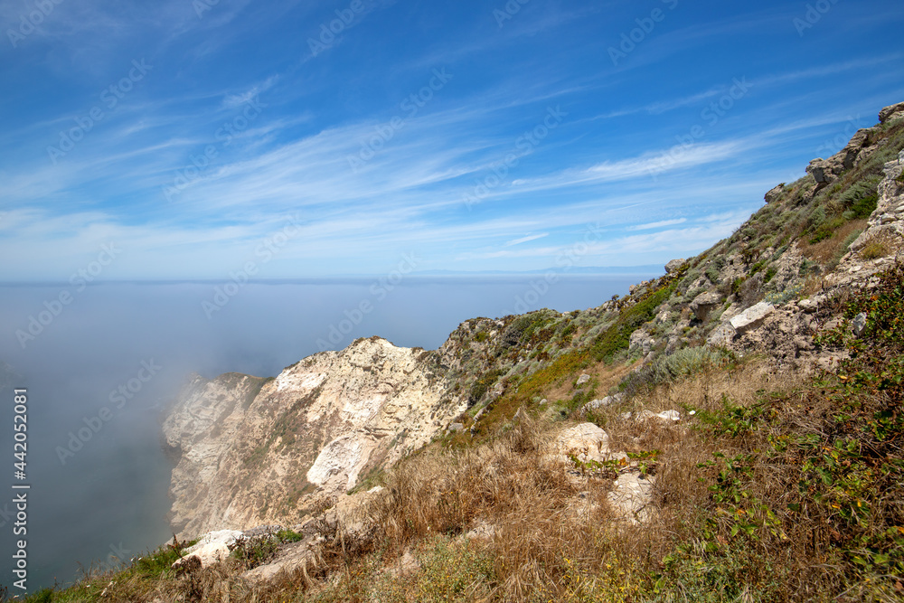 Inversion layer clouds misting over Potato Harbor on Santa Cruz Island with mist coming in under blue cirrus sky in the Channel Islands National Park offshore from Santa Barbara California USA