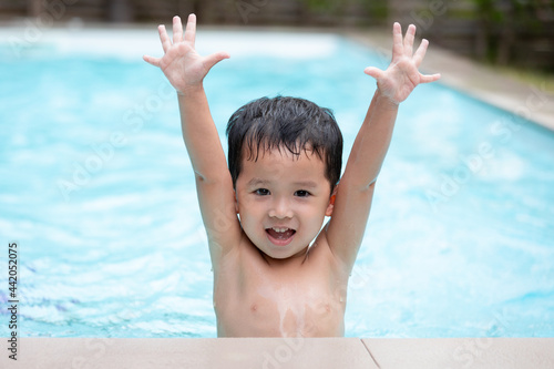 Portrait of asian little boy looking at camera and smiling while playing water in the swimming pool. Summer activity and childhood lifestyle concept. © pingpao