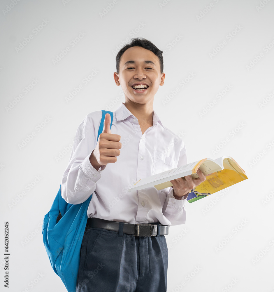 a boy wearing a junior high school uniform smiles while holding a book with thumbs up with an isolated background a boy wearing a junior high school uniform smiles while holding a book with thumbs up with an isolated background