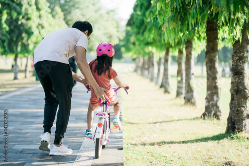 Fototapeta Naklejka Na Ścianę i Meble -  asian Father Teaching daughter To Ride Bike In the park