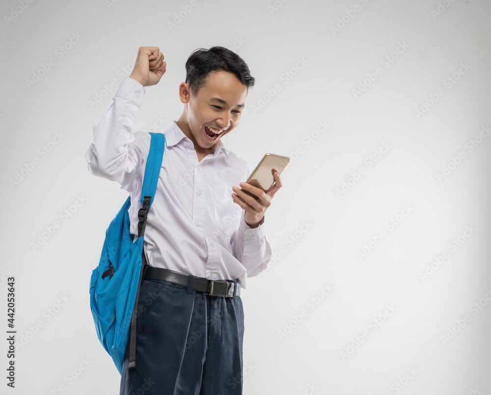 a boy wearing a junior high school uniform looking at a cellphone with an excited gesture with a backpack with an isolated background a boy wearing a junior high school uniform looking at a cellphone with an excited gesture with a backpack with an isolated background