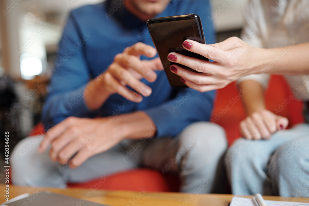Close-up image of businesswoman showing message on smartphone to her colleague at meeting Close-up image of businesswoman showing message on smartphone to her colleague at meeting