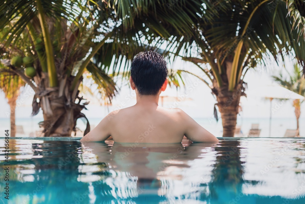 Asian happy man swimming and relax in swimming pool at resort hotel by the sea background on weekend vacation.Concept of happy solo travel.