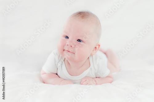 Three-month caucasian boy in white clothes lying on his belly on white blankets