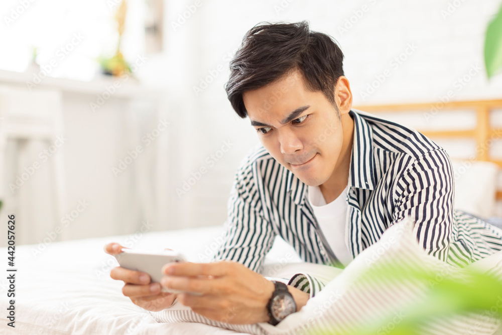Handsome young man in casual clothes lying on the bed and playing mobile phone games, with excited emotions and expressions Handsome young man in casual clothes lying on the bed and playing mobile phone games, with excited emotions and expressions
