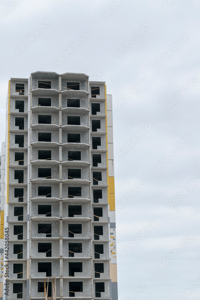 A multi-storey building under construction. Construction technology - panel housing construction. Window openings without glazing. Sky with clouds. Vertical layout. A multi-storey building under construction. Construction technology - panel housing construction. Window openings without glazing. Sky with clouds. Vertical layout.