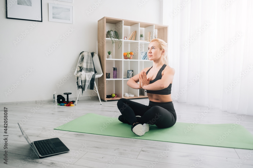 Online meditation. Harmony woman. Home yoga. Mental balance. Healthy body. Inspired lady black sportswear sitting lotus pose namaste hands laptop on floor in light room interior. Online meditation. Harmony woman. Home yoga. Mental balance. Healthy body. Inspired lady black sportswear sitting lotus pose namaste hands laptop on floor in light room interior.