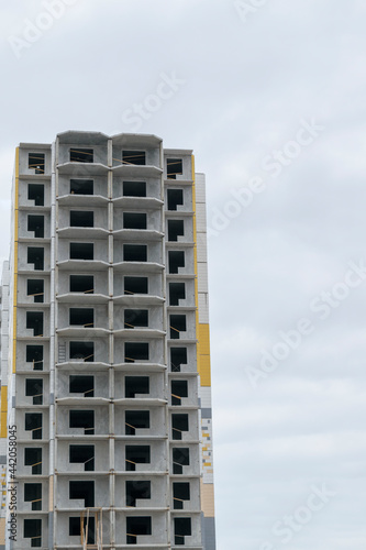 A multi-storey building under construction. Construction technology - panel housing construction. Window openings without glazing. Sky with clouds. Vertical layout.