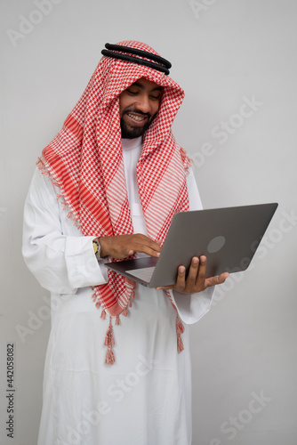 an arabian in a turban smiling while using a laptop computer on a plain background photo