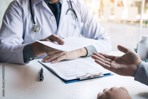 Asian male doctor talking in clinic room and handing a prescription to the patient. photo