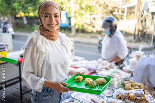 smiling a beautiful girl in a veil hold plastic tray selling various kinds of fried foods on the side of the road