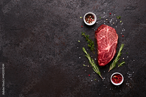 Fresh raw marbled beef rib eye steak, herbs and spices on black stone background, copy space photo