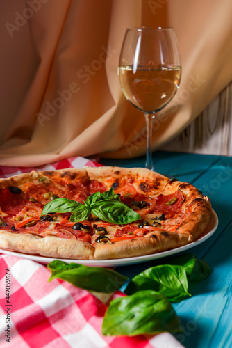 Fresh italian pizza with salami and black olives and other food on the background. Blue colored wooden table.