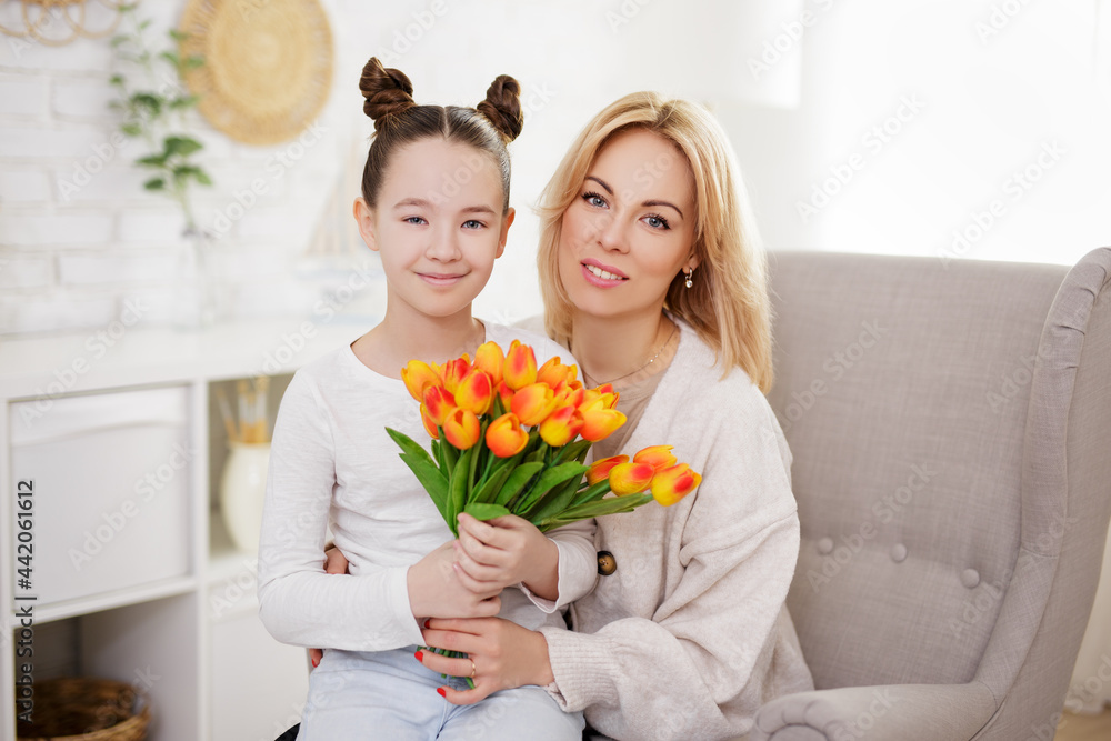 motherhood, family and mother's day concept - cute girl giving flowers to her mother in living room