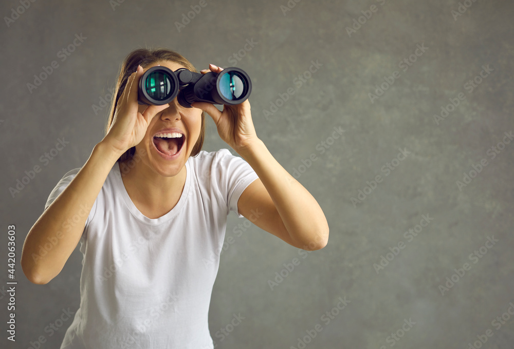 Young smiling woman looking through binoculars with happy face surprised expression studio headshot on grey background. Shock, surprise people emotion and spy on, search, find something concept Young smiling woman looking through binoculars with happy face surprised expression studio headshot on grey background. Shock, surprise people emotion and spy on, search, find something concept