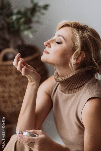 Young beautiful woman holds a bottle of perfume in her hands and inhales while enjoying the fragrance from her wrist. Soft selective focus.