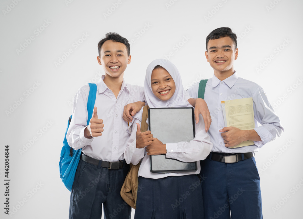 Three teenagers in junior high school uniforms holding a laptop computer with thumbs up when carrying school bag and a book on an isolated background Three teenagers in junior high school uniforms holding a laptop computer with thumbs up when carrying school bag and a book on an isolated background