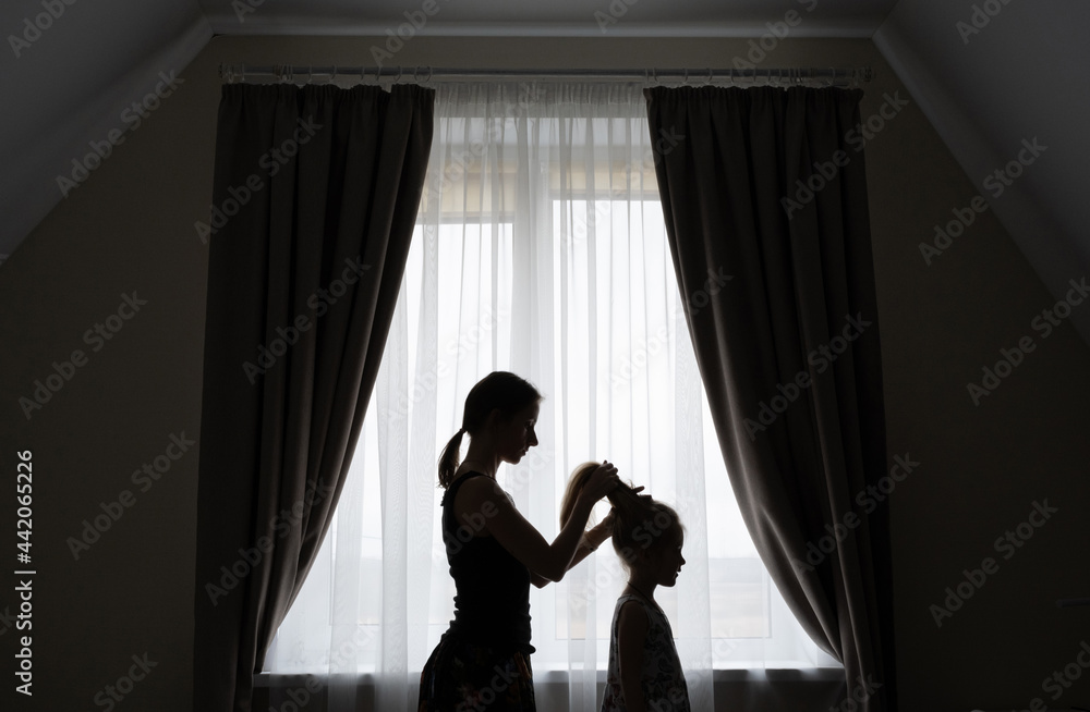 The silhouette of a caring mother combing her daughter's hair