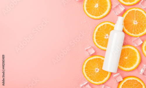 Top view photo of white spray bottle without label on orange slices ice cubes and water drops on isolated pastel pink background with blank space on the left