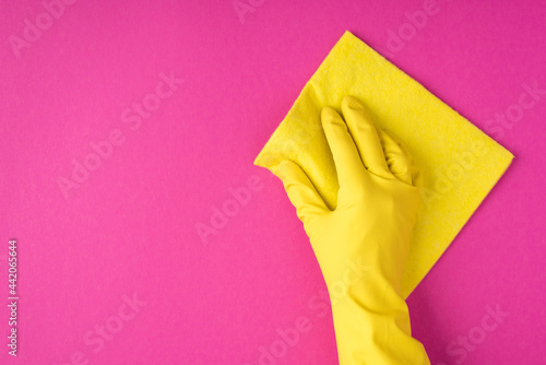Top view photo of hand in yellow glove using yellow viscose rag on isolated pink background with copyspace