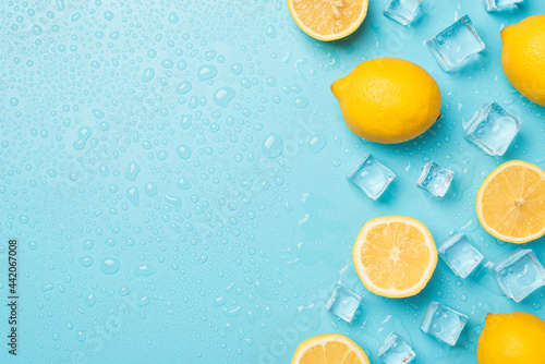 Above photo of yellow lemons cubes of ice and drops isolated on the blue background with empty space