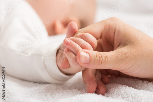 Closeup photo of newborn's small hand clenching mother's forefinger on isolated white textile background
