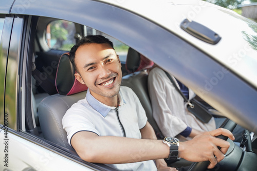 a young asian man laughing looking at the camera while driving in a car while passing on the road