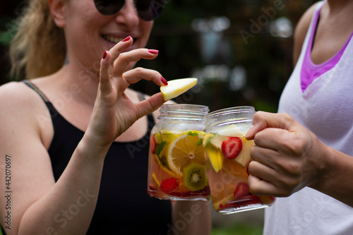 two young women with sunglasses, toast to health with detox drinks. Selective Focus Glasses