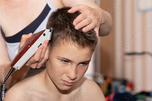 Cutting the hair of a boy, young guy at home due to the lockdown and quarantine coronavirus epidemic. Parents and relatives help each other get their hair without going to the hairdresser