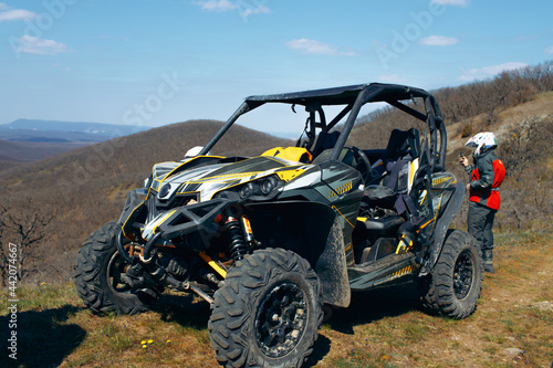 Buggy parked in mountains and driver in sport equipment standing behind photo
