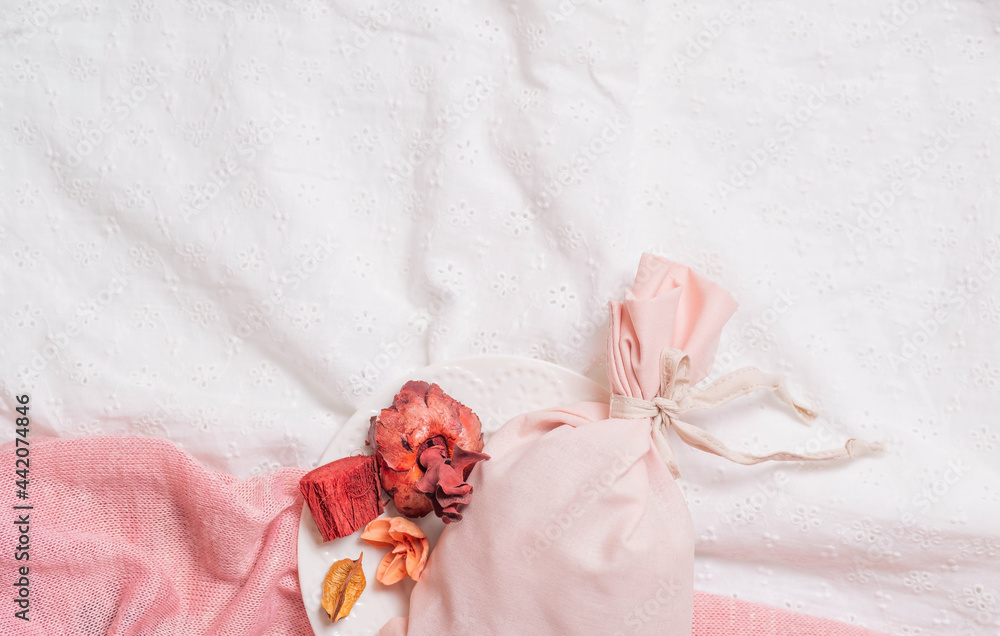 The bag of sachet with dry fragrant flowers rests on the white and pink fabric, the background. The bag of sachet with dry fragrant flowers rests on the white and pink fabric, the background.