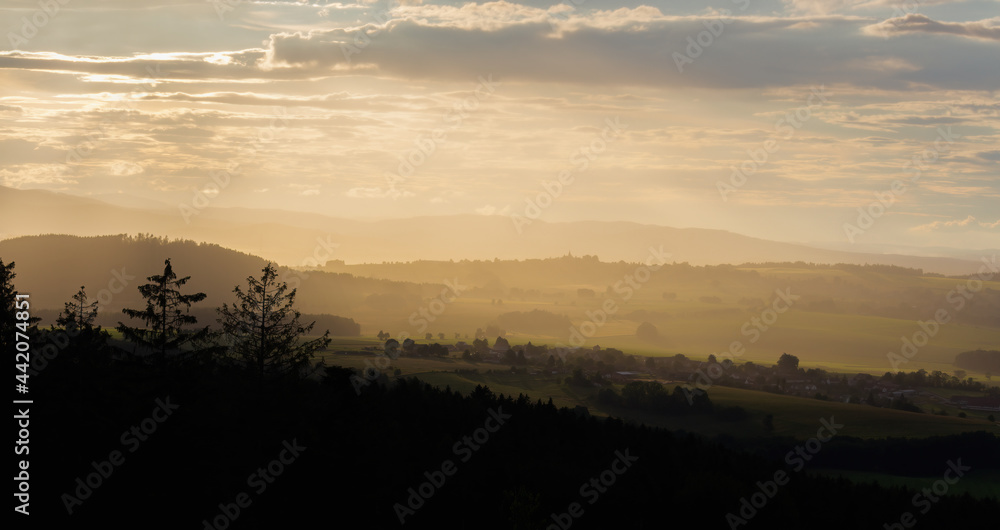 View to summer Czech valley with small vilage Besednice at sunset cloudy sky and rain haze. Silhouette landscape