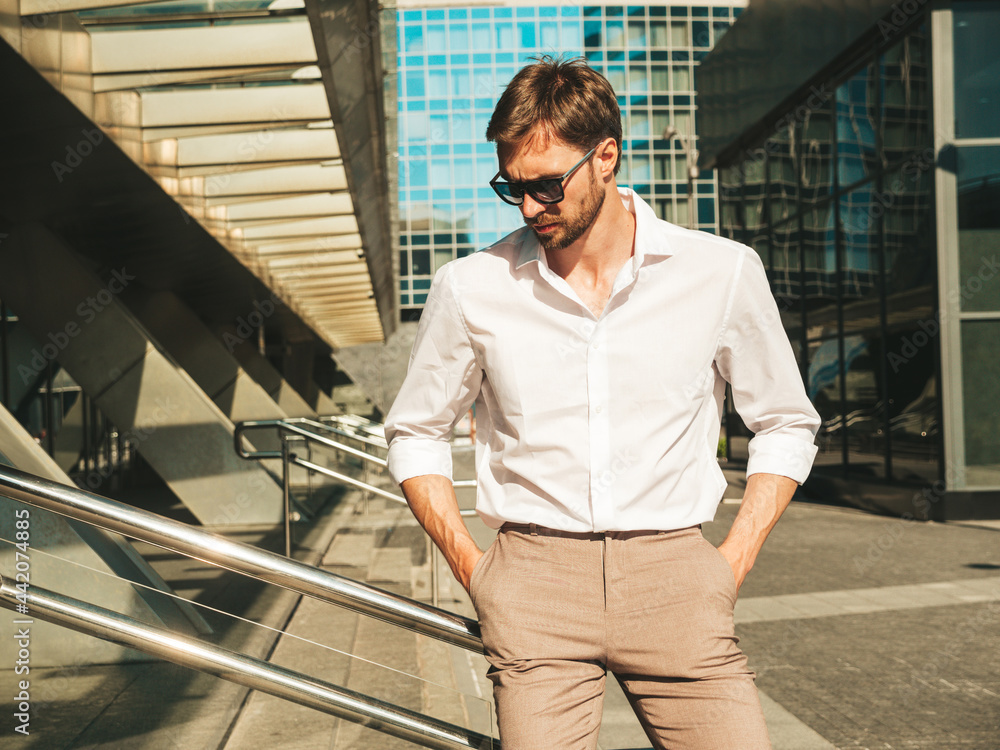 Portrait of handsome confident stylish hipster lambersexual model.Modern man dressed in white shirt. Fashion male posing in the street background near skyscrapers in sunglasses. Outdoors at sunset Portrait of handsome confident stylish hipster lambersexual model.Modern man dressed in white shirt. Fashion male posing in the street background near skyscrapers in sunglasses. Outdoors at sunset