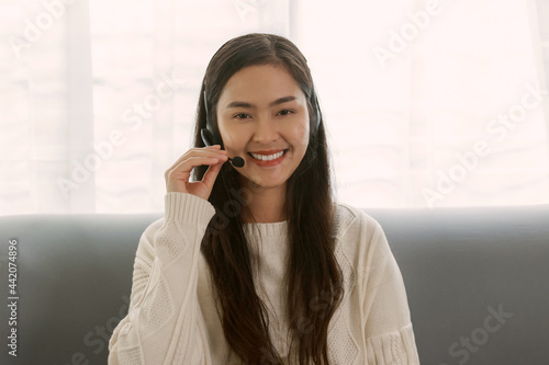 Young Attractive Smiley Asian woman wearing headset doing video chat in the living room. Asian instructor wearing headphone getting ready for online class at home.