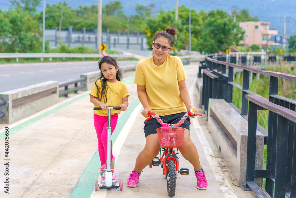 Little child girl to ride scooter with mother ride on small bicycle outdoor sports ground on sunny summer day. Active leisure and outdoor sport for children. Little child girl to ride scooter with mother ride on small bicycle outdoor sports ground on sunny summer day. Active leisure and outdoor sport for children.
