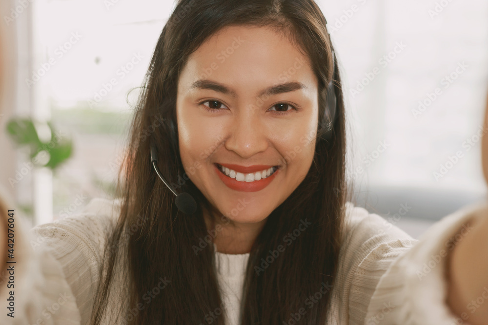 Young Attractive Smiley Asian woman wearing headset doing video chat in the living room. Asian instructor wearing headphone getting ready for online class at home. Young Attractive Smiley Asian woman wearing headset doing video chat in the living room. Asian instructor wearing headphone getting ready for online class at home.