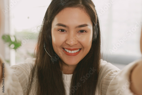 Young Attractive Smiley Asian woman wearing headset doing video chat in the living room. Asian instructor wearing headphone getting ready for online class at home.