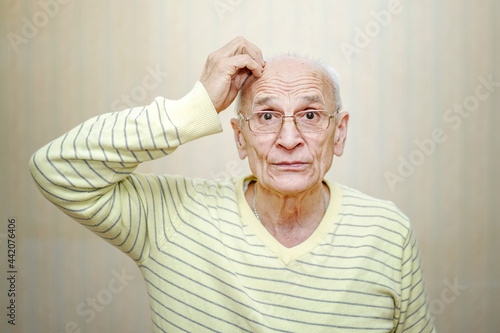 Senior man in eyeglasses touches head with hand and thinks of something.