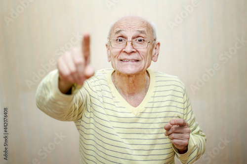 Aged old man wearing eyewear pointing finger up and smiling.